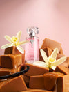 Caramel Temptress Eau De Parfum Intense 1.7 fl oz perfume bottle with vanilla flowers and caramel pieces on a pink background