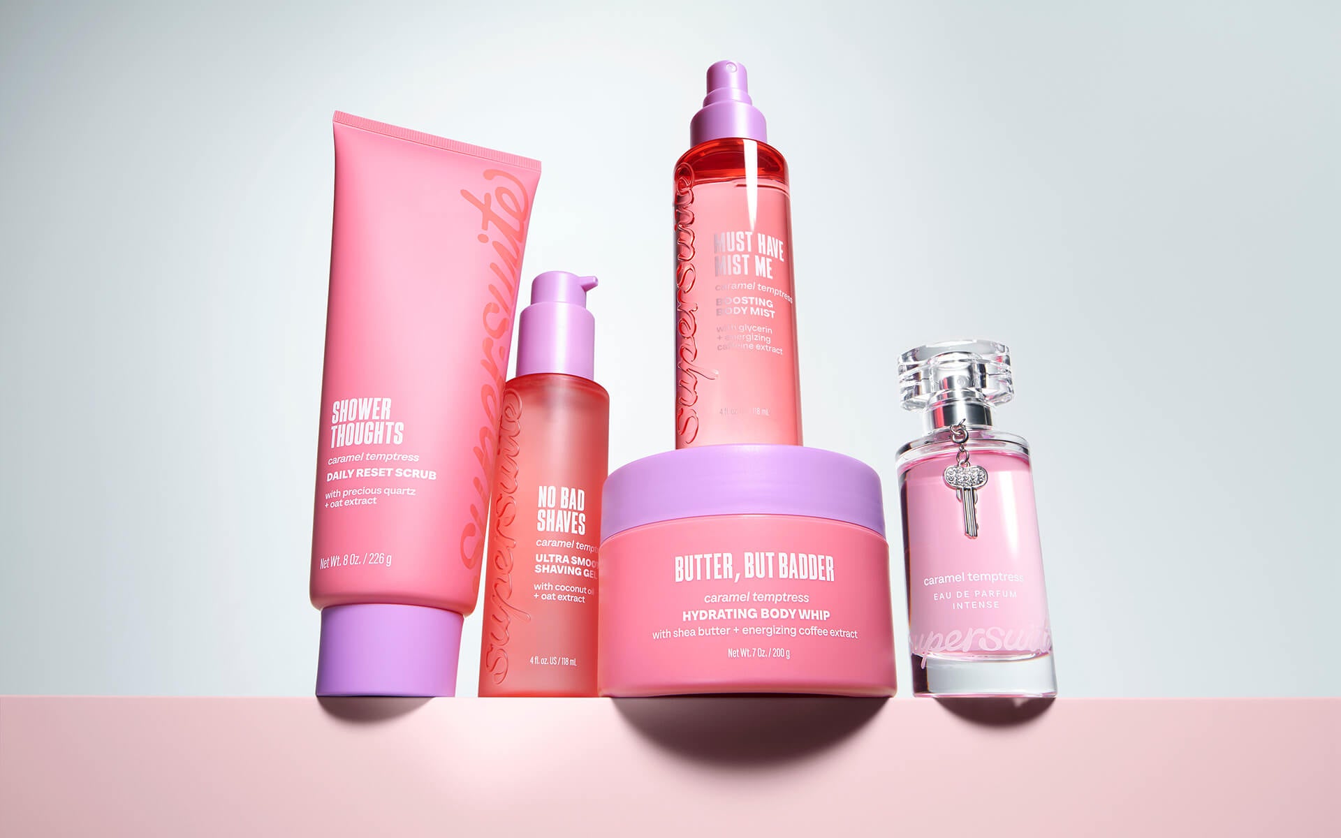 The complete SuperSuite Caramel Temptress bodycare line on a warm pink gradient background